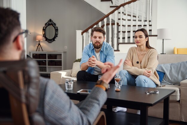 Feche acima do psicólogo masculino senta-se na cadeira e ouve casal jovem deprimido no escritório acolhedor elegante. Foco seletivo.