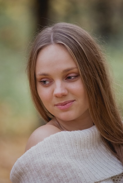 Feche acima do retrato de uma menina bonita na camisola branca perto das folhas de outono coloridas. Arte da mulher romântica. Modelo de ternura bonita sorrindo