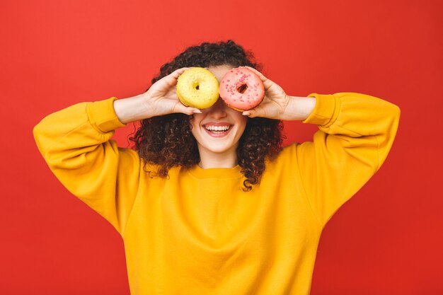 Foto feche acima do retrato de uma moça bonita satisfeita que come os anéis de espuma isolados sobre o fundo vermelho.