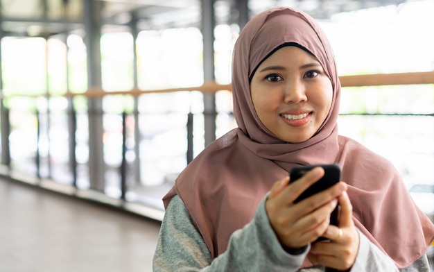 Feche acima do sorriso da mulher muçulmana e mantenha o telefone celular no tempo de relaxamento, conceito dos povos do estilo de vida