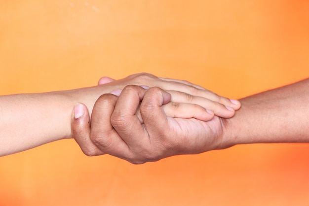 Foto feche acima dos pares que mantêm as mãos contra o fundo alaranjado.