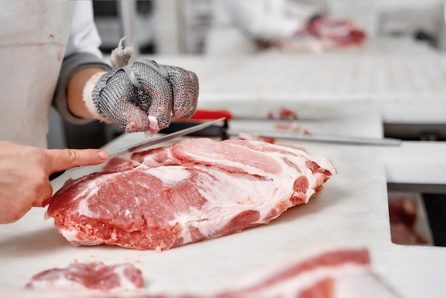 Foto feche acima dos pedaços de carne e mãos do trabalhador no corte das luvas.