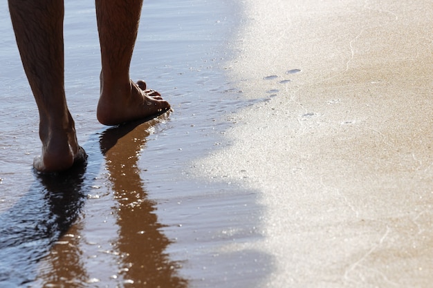 Feche acima nos pés moventes de um homem que anda na praia na tarde em koh mak em trat, tailândia.