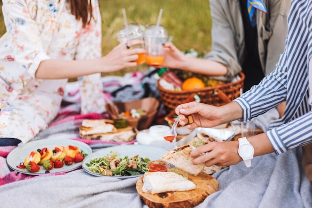 Feche as garotas passando tempo em um belo piquenique com variedade de comidas e bebidas saborosas na manta de piquenique no parque