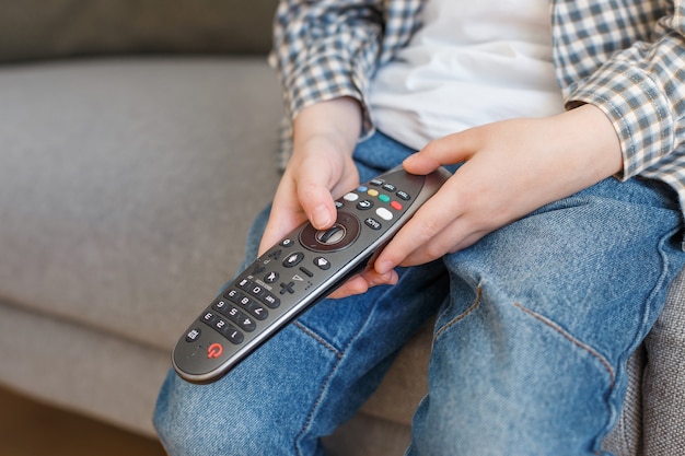 Feche as mãos da criança segurando o controle remoto da TV