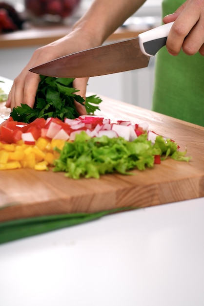 Feche as mãos da mulher cozinhando na cozinha. Dona de casa cortando salada fresca. Conceito de culinária vegetariana e saudável.