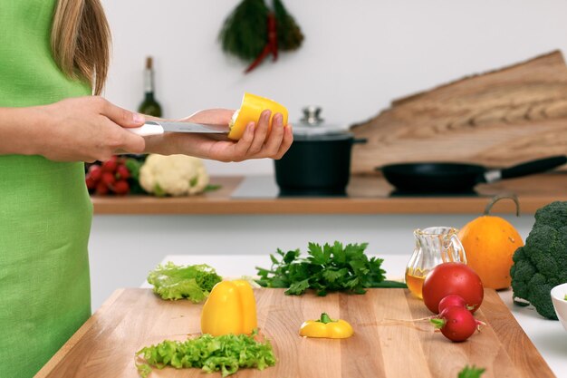 Feche as mãos da mulher cozinhando na cozinha. Dona de casa cortando salada fresca. Conceito de culinária vegetariana e saudável.