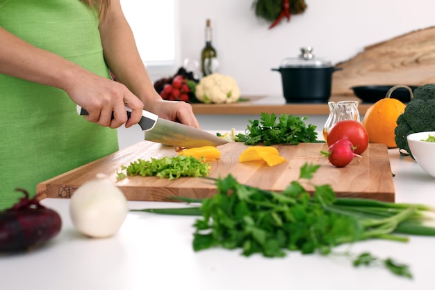 Feche as mãos da mulher cozinhando na cozinha. Dona de casa cortando salada fresca. Conceito de culinária vegetariana e saudável.