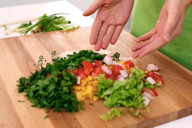 Feche as mãos da mulher cozinhando na cozinha. Dona de casa cortando salada fresca. Conceito de culinária vegetariana e saudável.