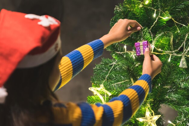 Foto feche as mãos da mulher decorando as luzes e enfeites da árvore de natal para comemorar em dezembro e na temporada de inverno