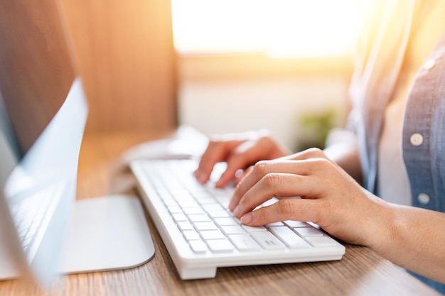 Feche as mãos da mulher digitando no teclado do computador desktop no escritório