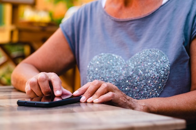Foto feche as mãos da mulher sênior enquanto digita no celular senhora moderna idosa sentada ao ar livre no café desfrutando de tecnologia e mídia social