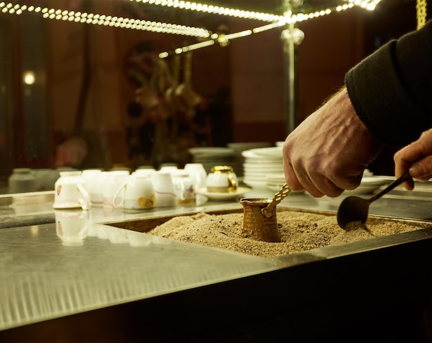 Feche as mãos de um homem cozinhando café turco na quente areia dourada.