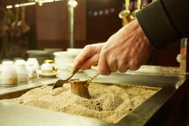 Feche as mãos de um homem cozinhando café turco na quente areia dourada.