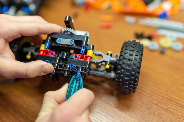 Feche as mãos de um menino brincando com o construtor fazendo carro ou robô Criança brincando com o construtor tecnológico