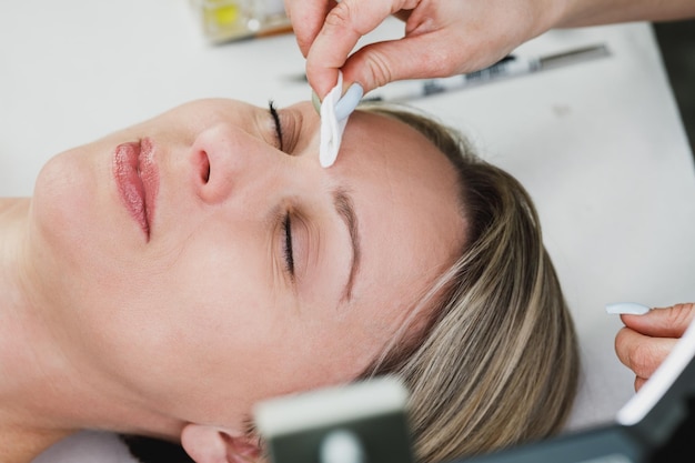 Feche as mãos de uma esteticista preparando o modelo para o procedimento de laminação de sobrancelha no salão de beleza.