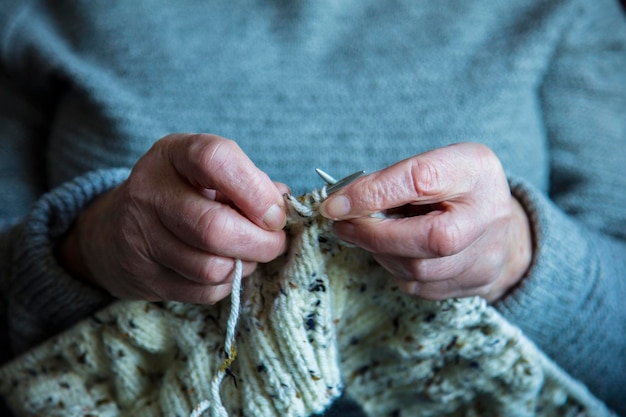 Feche as mãos de uma mulher mais velha tricotando um jumper