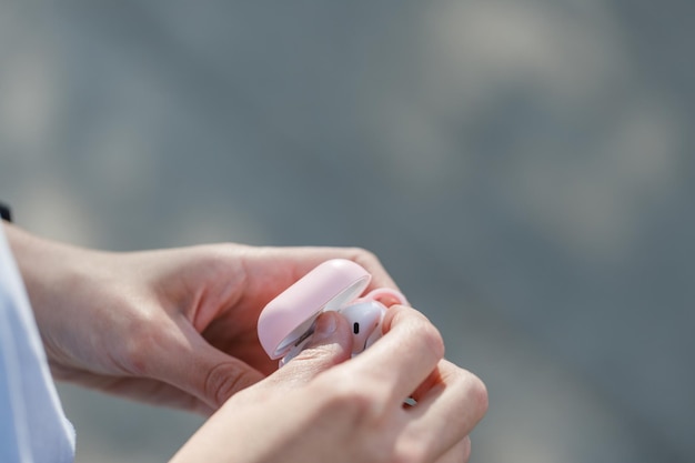 Feche as mãos de uma mulher tirando os fones de ouvido do estojo andando na rua