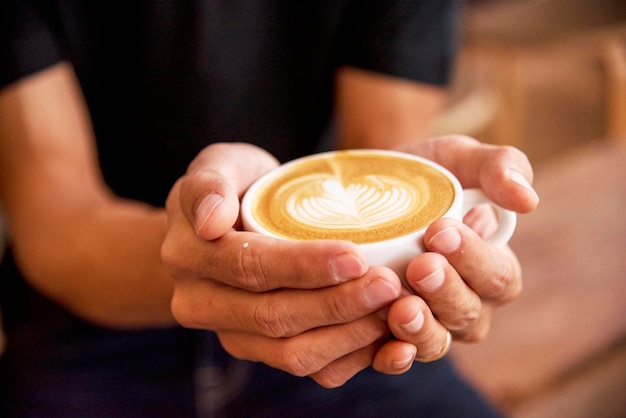 Foto feche as mãos do homem segurando uma xícara de café latte art na cafeteria caneca de café quente nas mãos do homem milk latte art fresco relaxe na hora da manhã