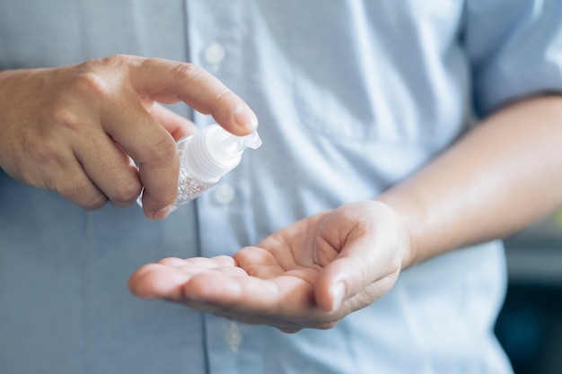 Feche as mãos do homem usando o dispensador de gel desinfetante para as mãos.