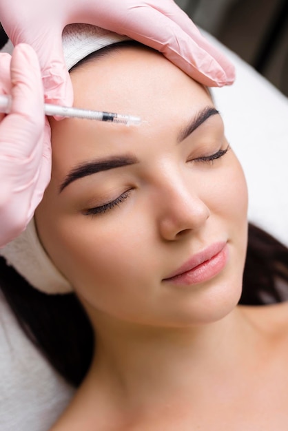 Feche as mãos do jovem cosmetologista injetando botox no rosto feminino ela está de pé e sorrindo a mulher está fechada os olhos com relaxamento