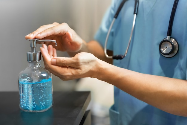 Foto feche as mãos do médico usando gel de álcool desinfetante para limpeza e desinfecção coronavirus, covid-19 antes de trabalhar na sala médica.