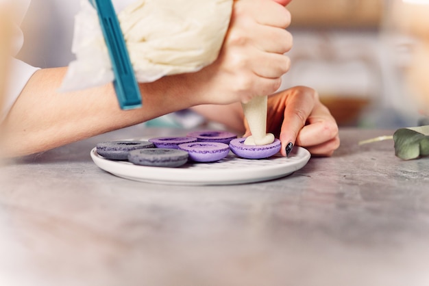 Feche as mãos do padeiro com saco de confeitaria, espremendo o creme para conchas de macarons.