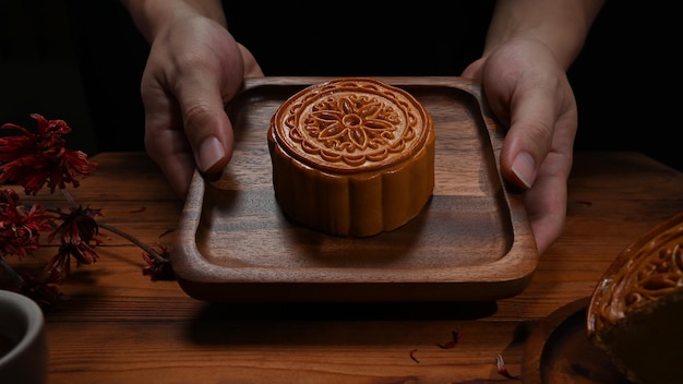 Feche as mãos segurando uma bandeja de madeira com bolo de lua Festival do meio do outono Comida tradicional chinesa e sobremesa