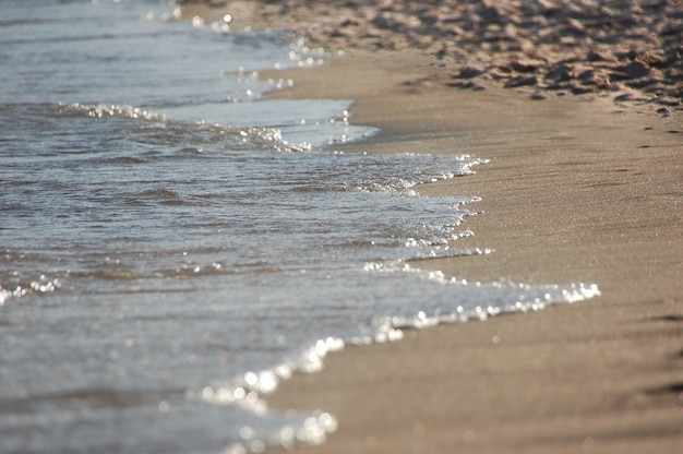 Feche as ondas de água do mar azul na praia de areia.