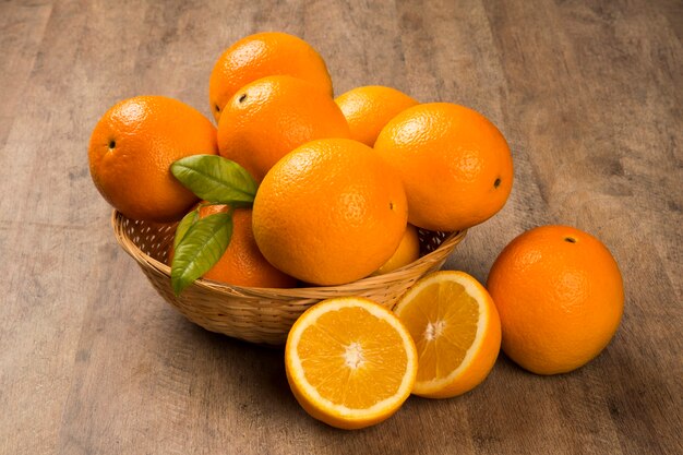 Feche de algumas laranjas em uma cesta sobre uma superfície de madeira. fruta fresca.