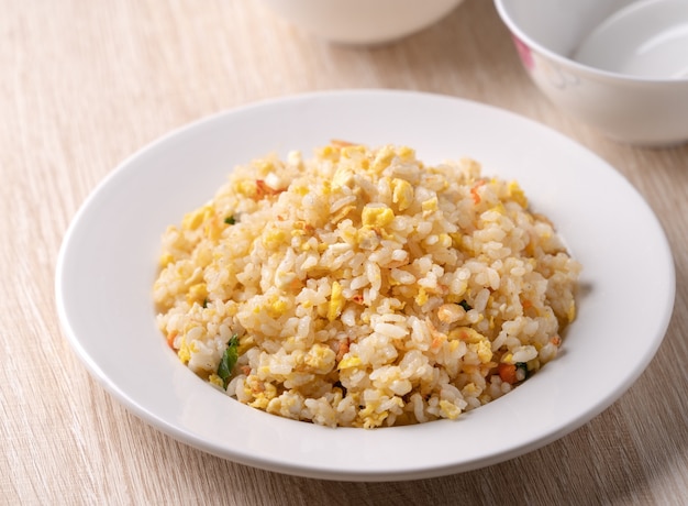 Feche de arroz frito chinês com sergestid Sakura camarão em chapa branca no fundo da mesa de madeira brilhante.