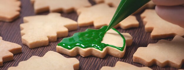 Feche de desenho biscoito de açúcar de árvore de Natal de gengibre no fundo da mesa de madeira com glacê verde, conceito de celebração do feriado.