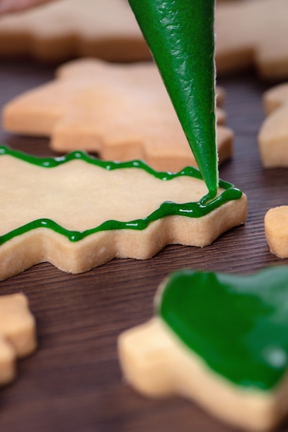 Feche de desenho biscoito de açúcar de árvore de Natal de gengibre no fundo da mesa de madeira com glacê verde, conceito de celebração do feriado.
