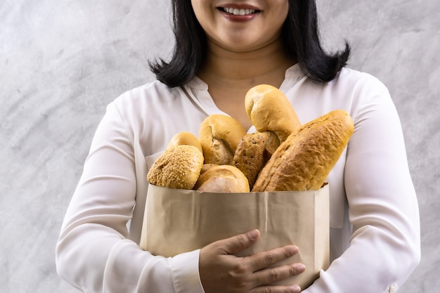 Feche de dona de casa de mulher sorriso asiático segurando pão variado em saco de papel descartável. Comida de padaria e mercearia de bebida e conceito de estilo de vida de vida doméstica para entrega.