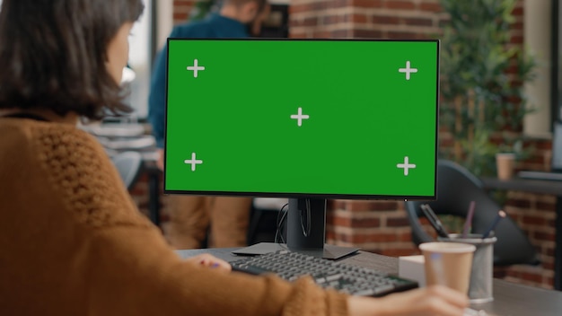 Feche de funcionário usando computador com tela verde na mesa. Mulher de negócios usando monitor com fundo isolado e modelo de maquete para chroma key em exposição. Pessoa com tecnologia