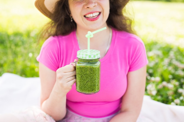 Feche de jovem divirta-se no parque e beba smoothies verdes em um piquenique.