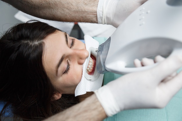 Foto feche de jovem recebendo um tratamento de clareamento de dentes em um dentista.