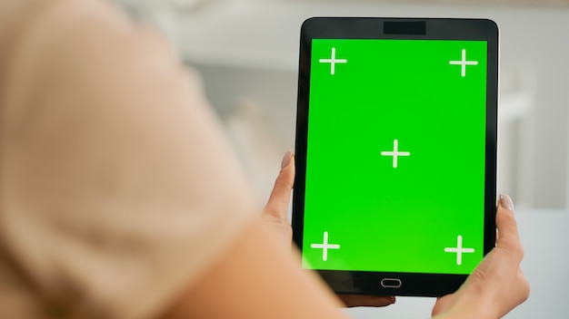 Feche de mãos de mulher segurando um computador tablet com simulação de visor de chave croma de tela verde. Freelancer sentado na mesa do escritório na sala de estar trabalhando com um dispositivo isolado para um projeto de estilo de vida online