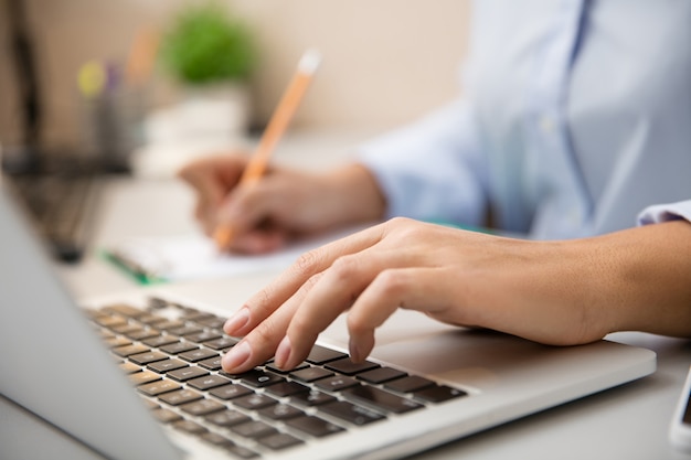 Feche de mãos femininas digitando. Trabalho remoto em casa. Local de trabalho em home office com PC, dispositivos e gadgets. Conceito de ensino à distância, isolamento, negócios femininos, compras online, conferência.