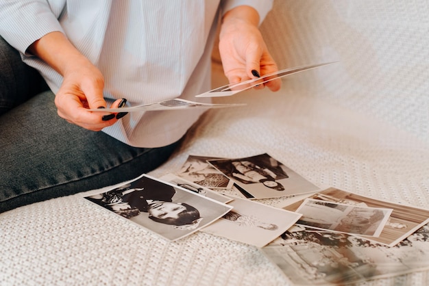 Feche de mãos femininas segurando fotos retrô de família antigas, mulher caucasiana olhando fotografias vintage lembrando e nostálgico sentado no sofá dentro de casa. Foco seletivo