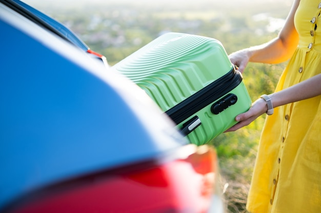 Feche de mãos femininas tirando a mala verde da mala do carro. Conceito de viagens e férias.