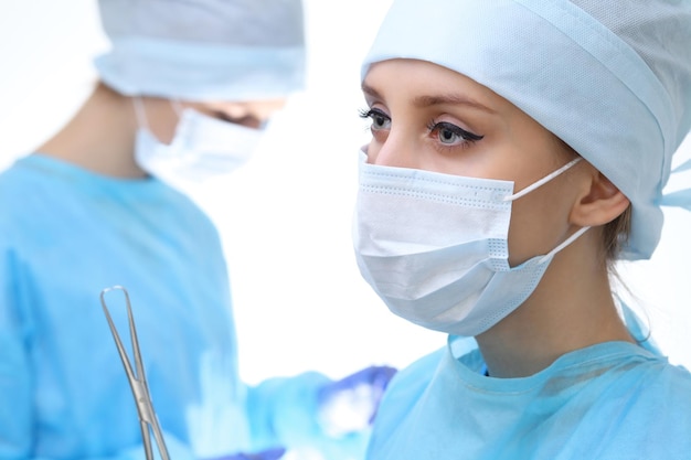 Feche de mulher cirurgiã olhando para a câmera enquanto colegas atuando em segundo plano na sala de operação, isolado. Conceito de cirurgia e medicina