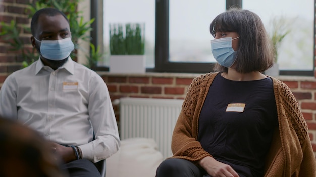 Feche de mulher com máscara facial participando de uma sessão de terapia em grupo. Pessoa conversando com pessoas com dependência de álcool, pedindo orientação e apoio durante a pandemia de coronavírus.
