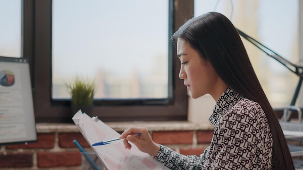 Feche de mulher comparando gráficos em papéis e computador. Funcionário da empresa trabalhando no projeto de negócios e planejando a estratégia de marketing no escritório de inicialização. Pessoa segurando documentos