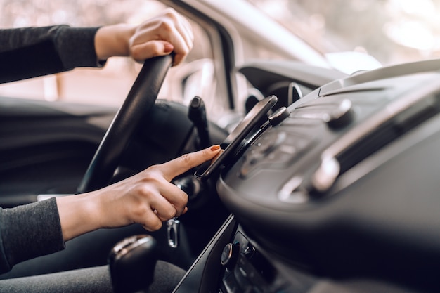 Feche de mulher grávida caucasiana, dirigindo o carro e ligar gps no telefone inteligente.