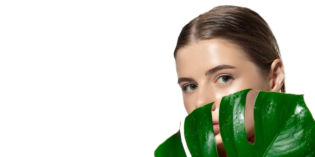 Feche de mulher jovem e bonita com folhas verdes sobre fundo branco. Conceito de cosméticos, maquiagem, tratamento natural e ecológico, cuidados com a pele. Pele brilhante e saudável, moda, saúde.