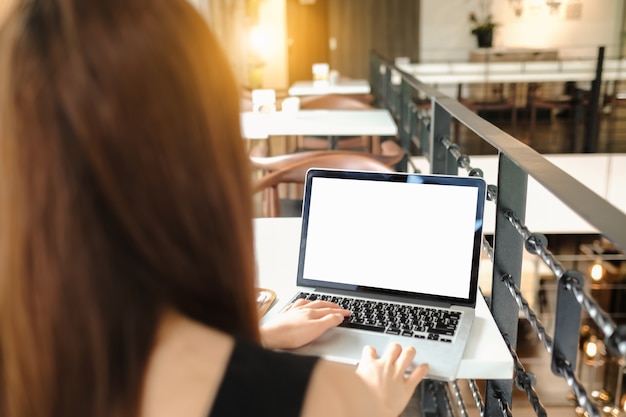 Feche de mulher usando telefone celular e laptop, enviando massagens dentro do café. Tomando banho de sol. Telefone com tela preta, mensagens de texto, chamadas de vídeo.