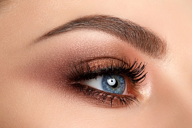 Feche de olhos de mulher azul com lindo marrom com maquiagem de olhos esfumados de tons de vermelho e laranja. a moda moderna compõe.