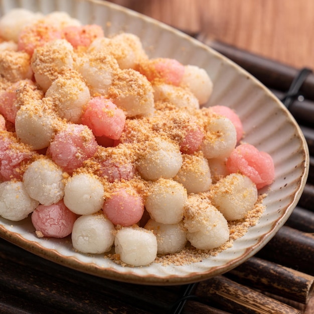 Feche de tangyuan vermelho e branco frito (tang yuan, bolinhos de arroz glutinoso) com pó de amendoim no fundo da mesa de madeira para comida do festival do solstício de inverno.