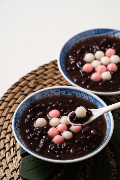 Feche de tangyuan vermelho e branco (tang yuan, bolas de bolinho de arroz glutinoso) com sopa de feijão vermelho doce em uma tigela no fundo da mesa branca para comida do festival do solstício de inverno.